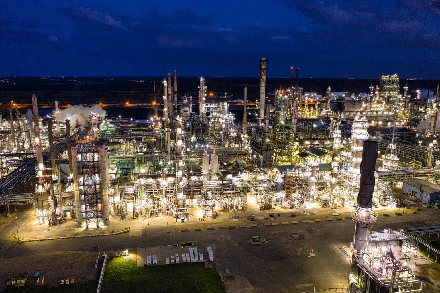 Oil price data displayed on a trading screen with crude oil refinery in background