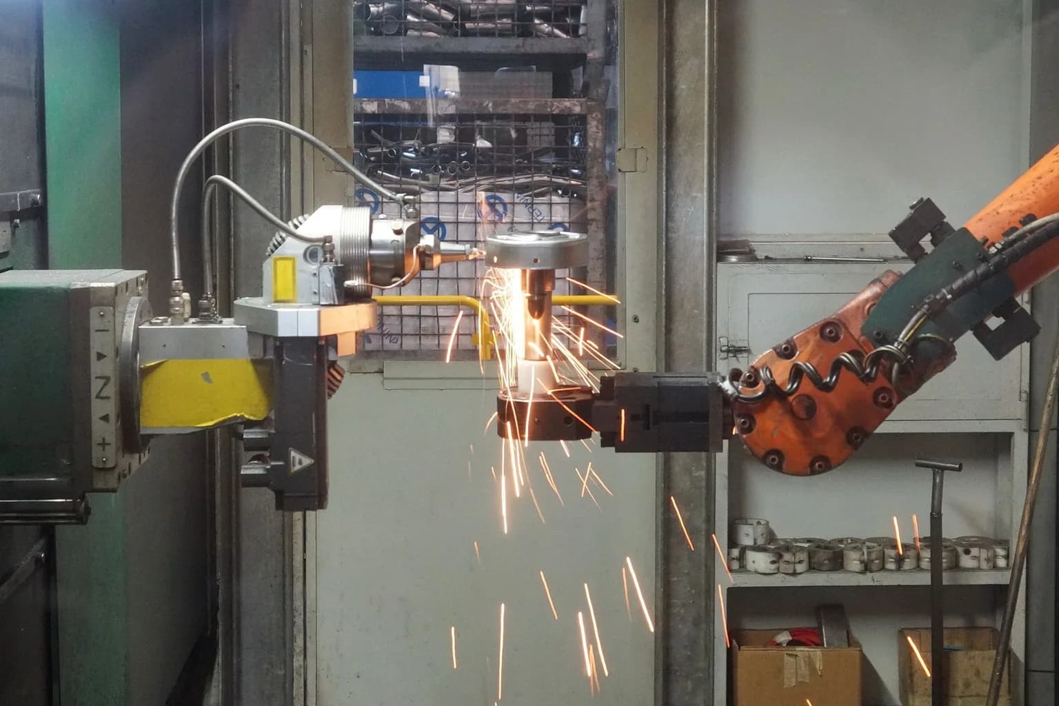 A Fanuc industrial robotic arm performing a welding operation on a metal workpiece in a factory setting