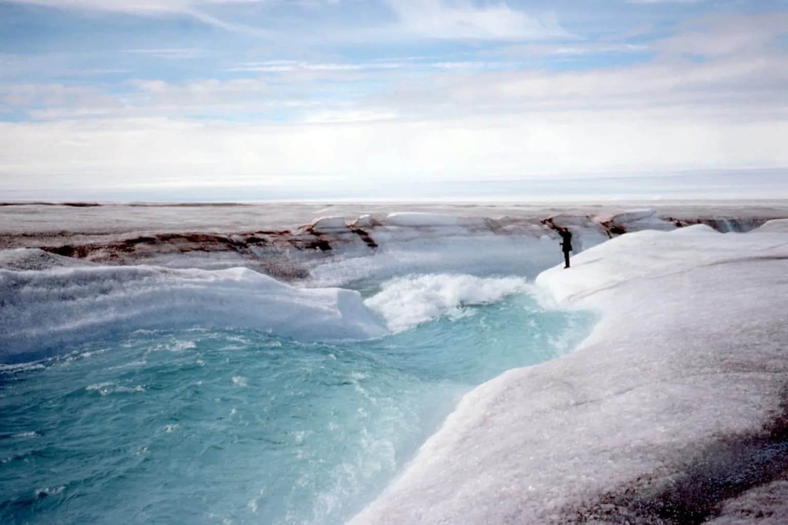 A glacier with meltwater flowing from its base into a river valley below