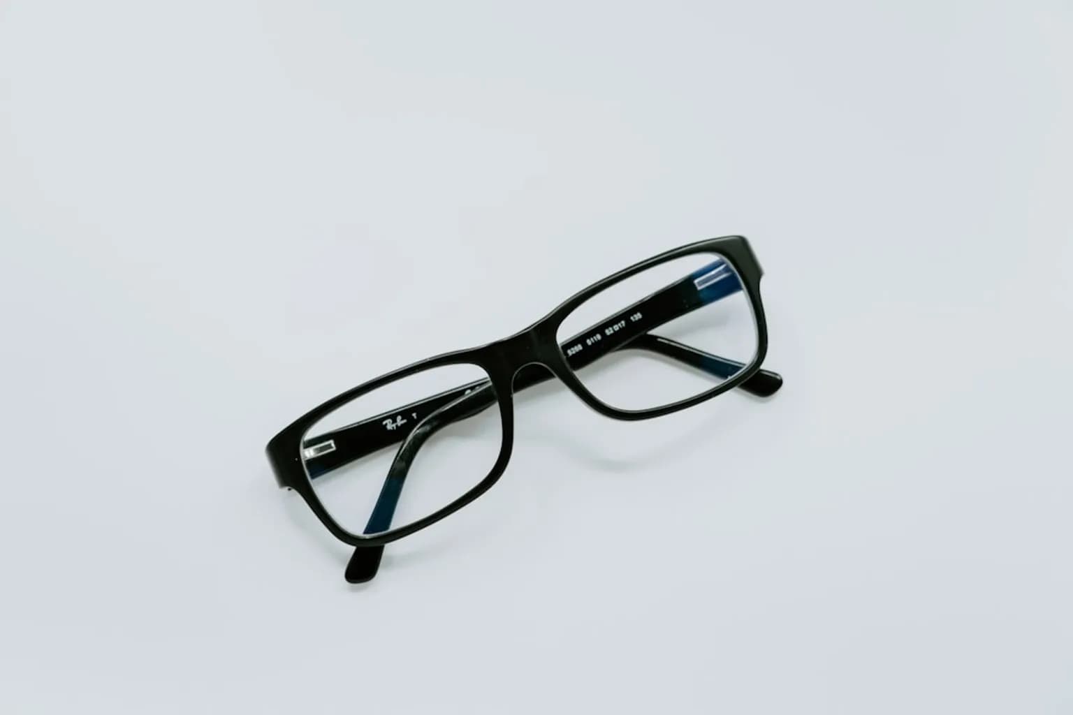 A pair of Ray-Ban Meta smart glasses on a white surface, showing the small camera lens on the frame